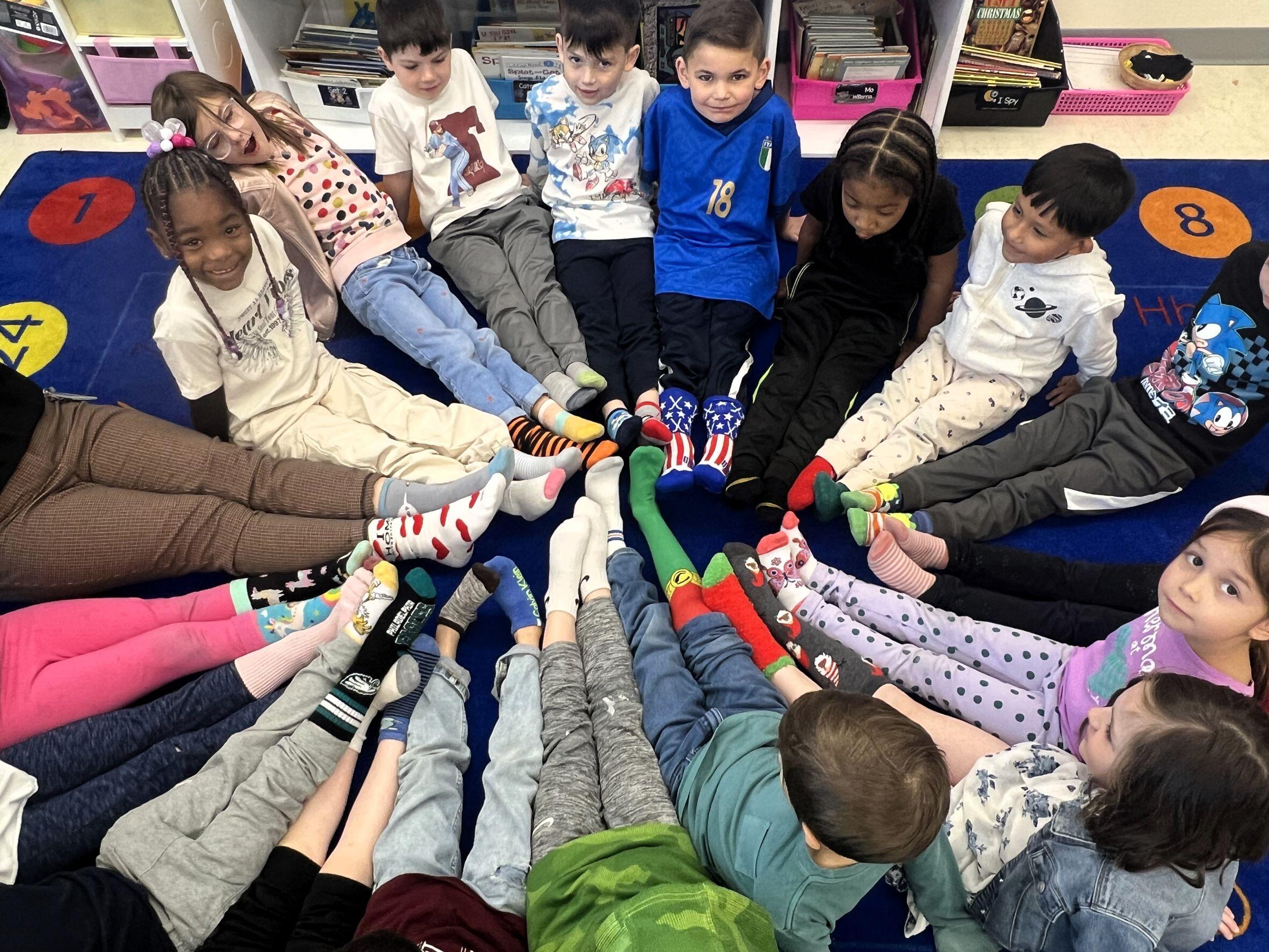 Enf- Class and teacher sitting on the floor in a circle with their legs outstretched, so their stocking feet at in the middle. From Crazy sock day