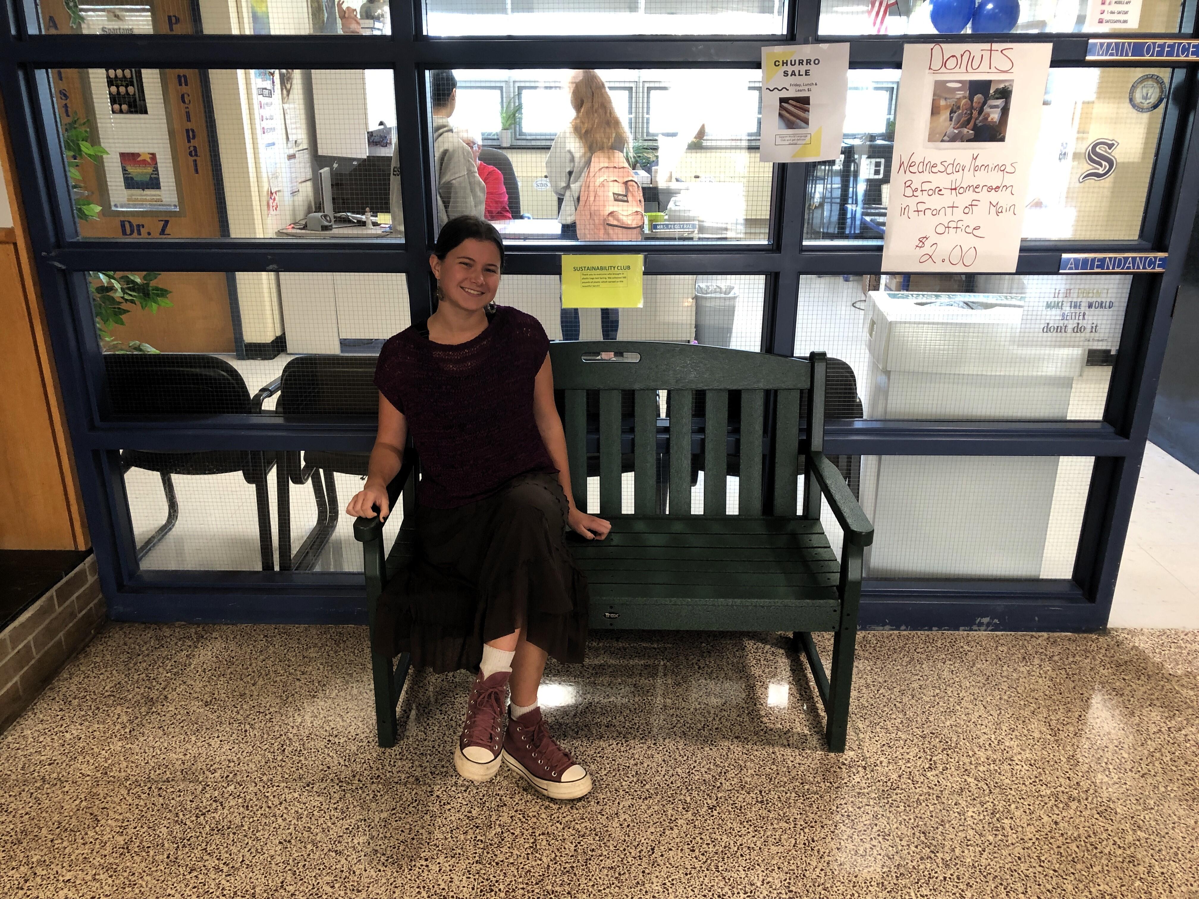 Student sitting on green bench in front of main office