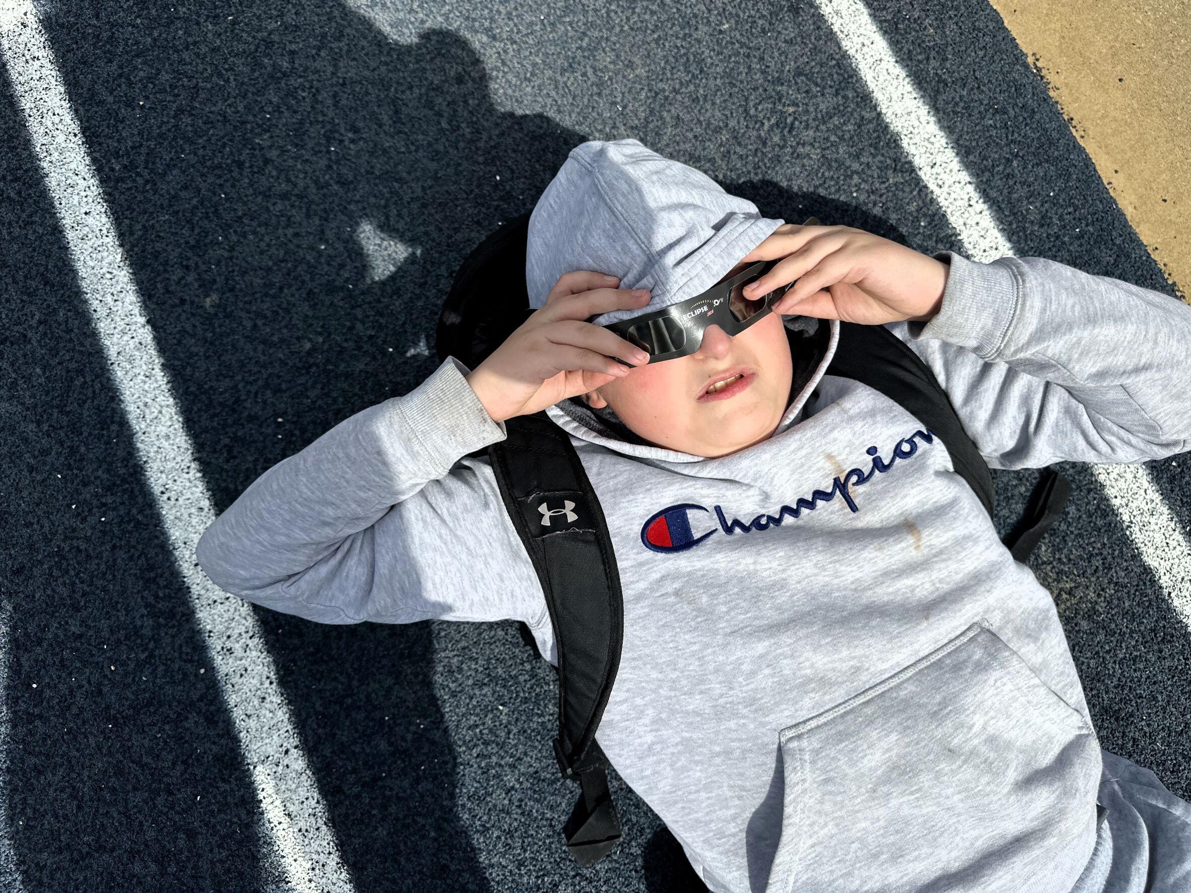 Student laying down on the track wearing his eclipse glasses looking at the sun